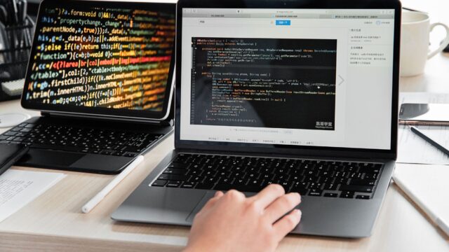 A developer writing code on a laptop, displaying programming scripts in an office environment.