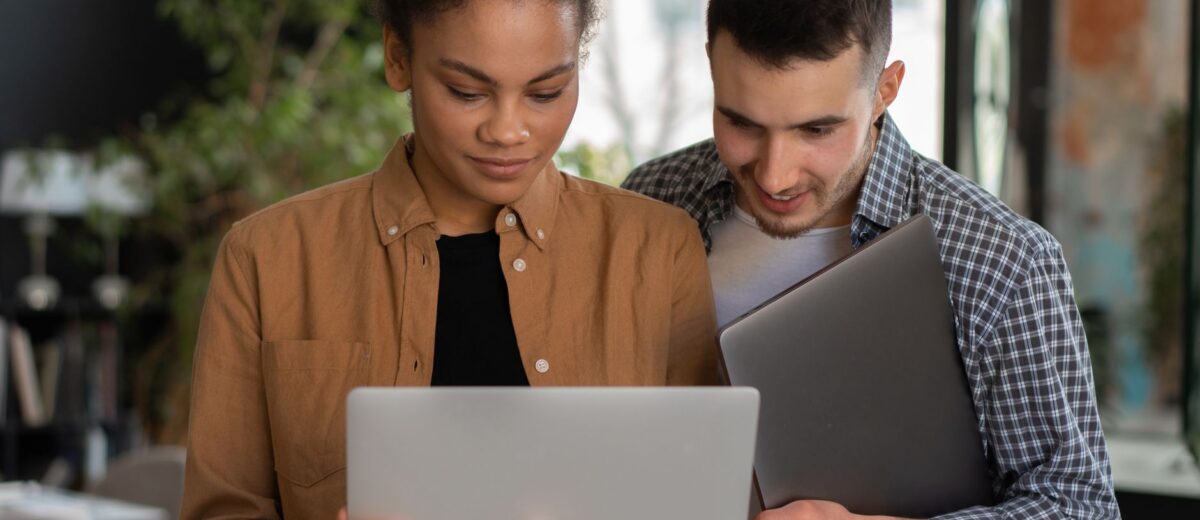 Two young professionals collaborating on a laptop in a modern office setting.