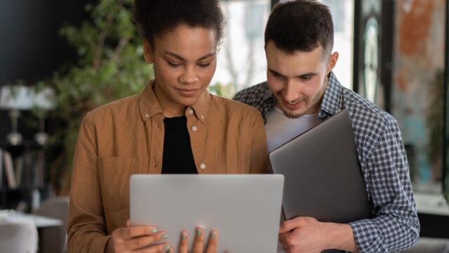 Two young professionals collaborating on a laptop in a modern office setting.