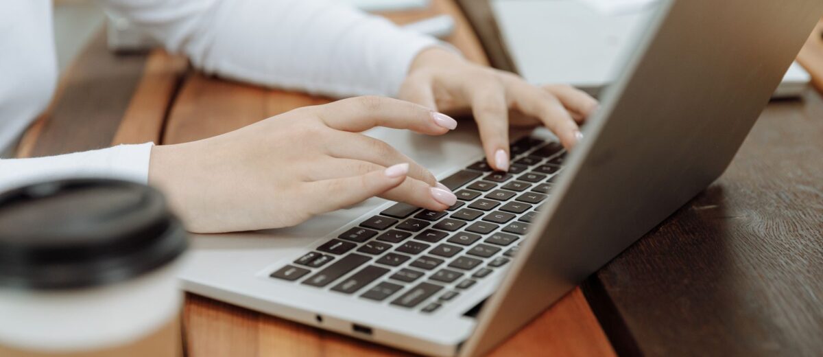 Close-up of a woman's hands typing on a laptop next to a coffee cup in a casual setting.