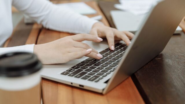 Close-up of a woman's hands typing on a laptop next to a coffee cup in a casual setting.