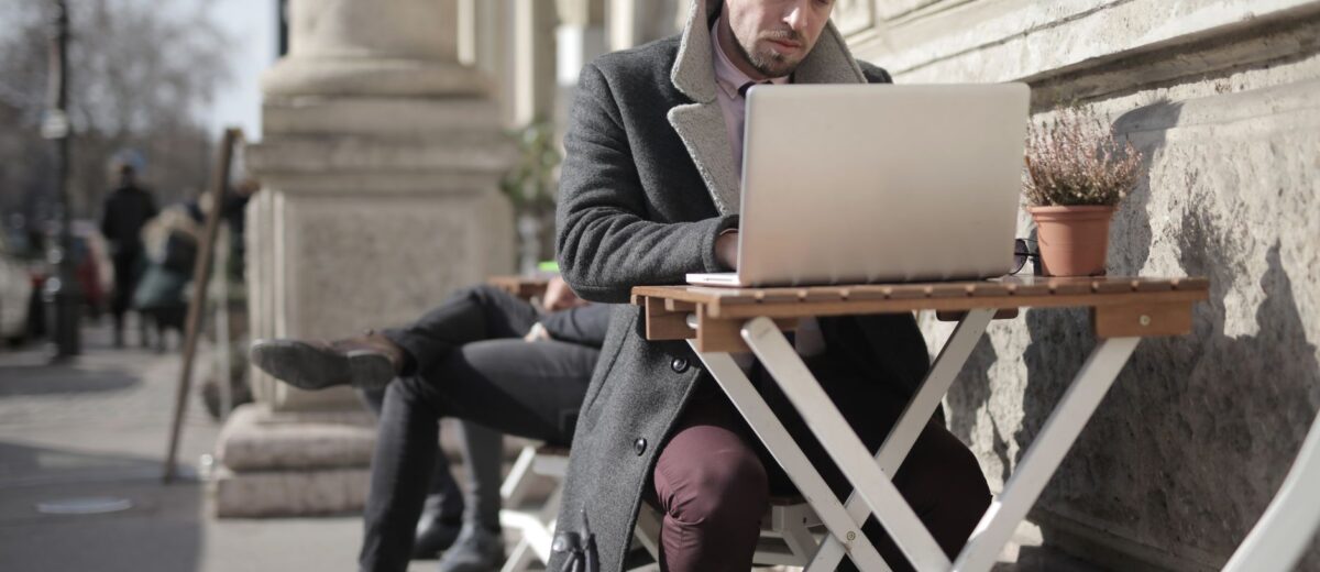 Freelancer working on laptop outdoors in urban area, embracing remote work lifestyle.
