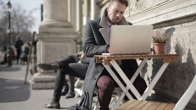 Freelancer working on laptop outdoors in urban area, embracing remote work lifestyle.