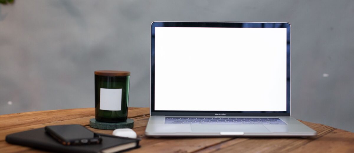 A modern workspace featuring a blank laptop screen, notebook, and candle on a wooden table.