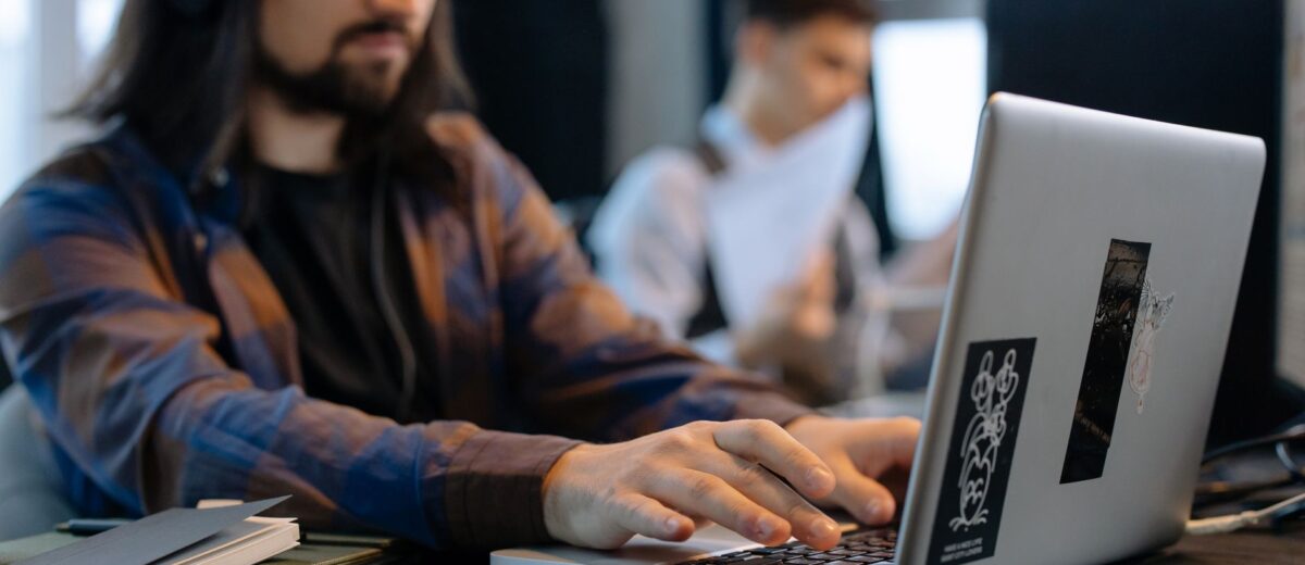 A man wearing headphones focused on typing at his laptop in a contemporary office setting.
